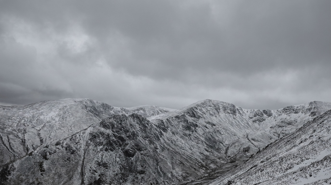 Snow-covered mountain ridges under heavy grey cloud in low winter light